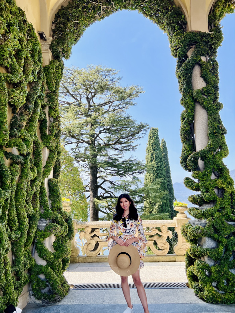 Woman in floral yellow dress under the green-laced columns of Villa del Balbianello, Lenno, Northern italy