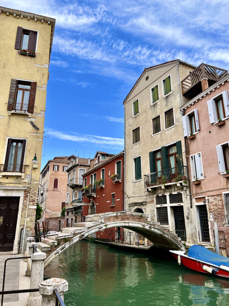 Bridge without rails above a green canal of water surrounded by yellow, pink, and red buildings in Venice, Northern Italy