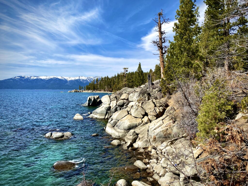 Lake Tahoe landscape with turquoise waters, rocks, snow-capped mountains, and pine trees